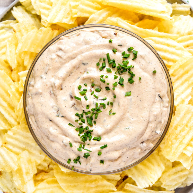 homemade roasted onion dip in a bowl with chives and potato chips on the side.