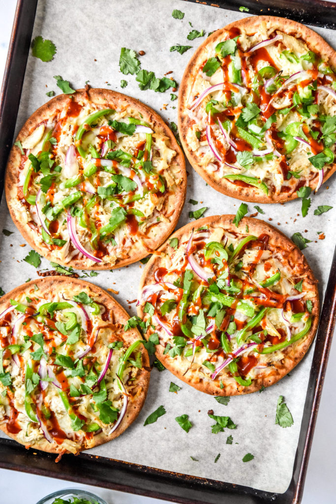 baked barbecue chicken flatbread pizzas on a sheet pan with cilantro on top.