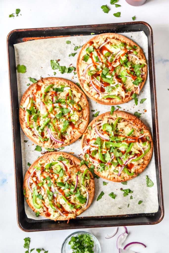 baked barbecue chicken flatbread pizzas on a sheet pan with cilantro on top.