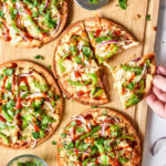 barbecue chicken flatbread pizzas on a cutting board one piece being removed.