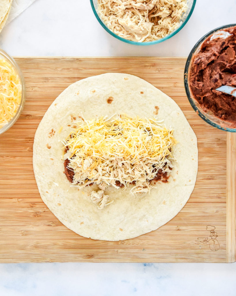 a tortilla on a cutting board with beans chicken and cheese inside.
