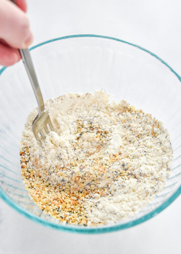 mixing dry ingredients together in a glass bowl including flour and everything bagel seasoning.