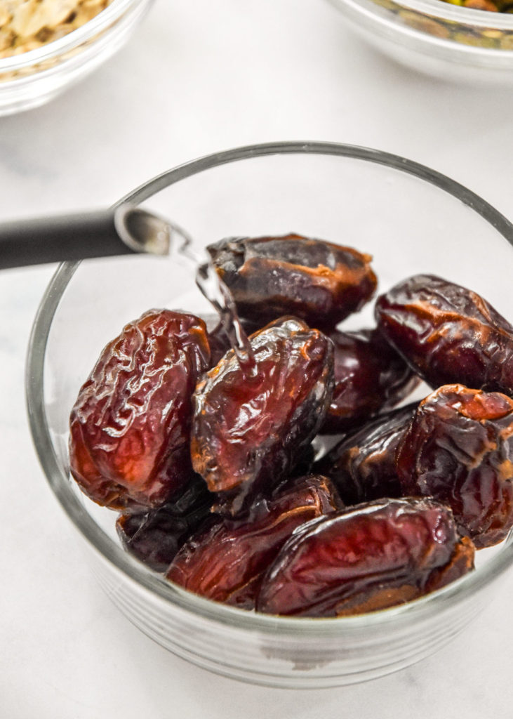 pouring hot water on large medjool dates in a glass bowl.