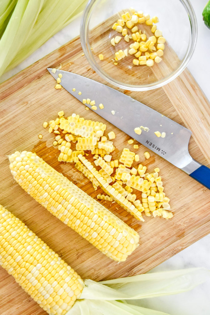 using a knife and cutting board to cut corn on the cob.