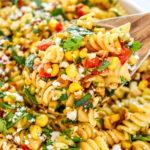 a scoop of pan roasted corn pasta salad in a wooden spoon.