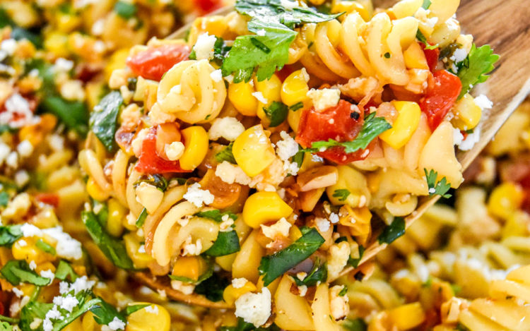 a scoop of pan roasted corn pasta salad in a wooden spoon.