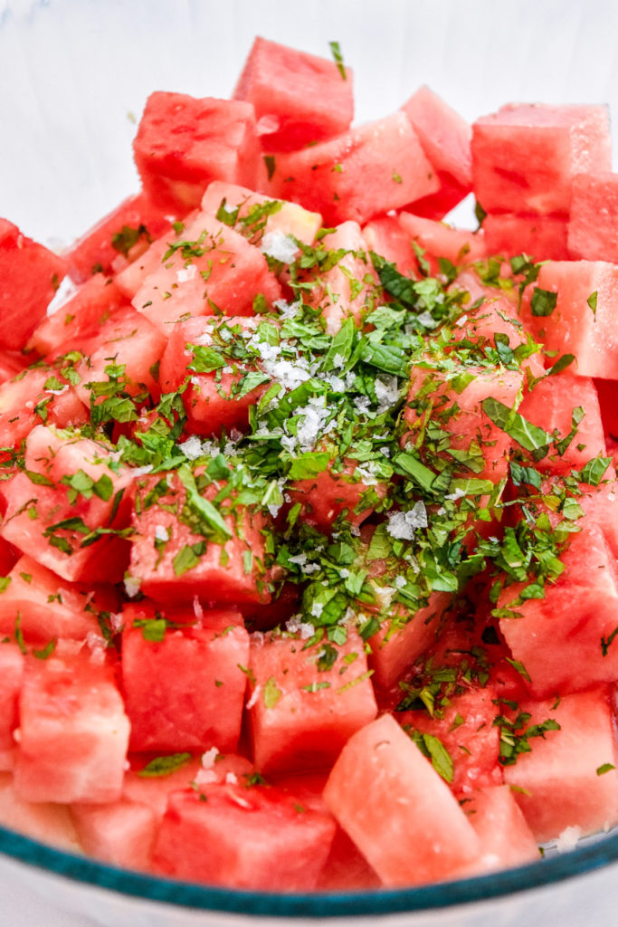chopped mint and sea salt on top of watermelon cubes in a bowl.