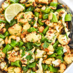 chili lime roasted cauliflower salad in a bowl with cilantro, cashews and a slice of lime on top.