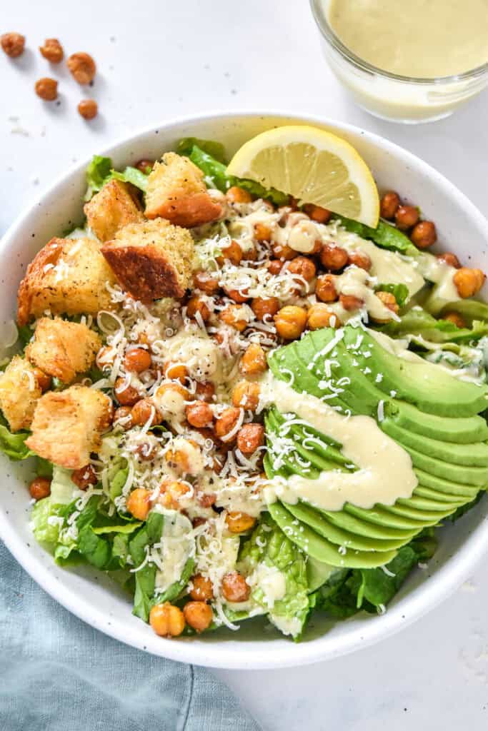 roasted chickpea caesar salad with avocado and croutons in a white bowl.