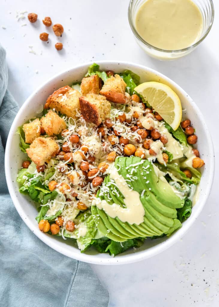 roasted chickpea caesar salad with avocado and croutons in a white bowl.