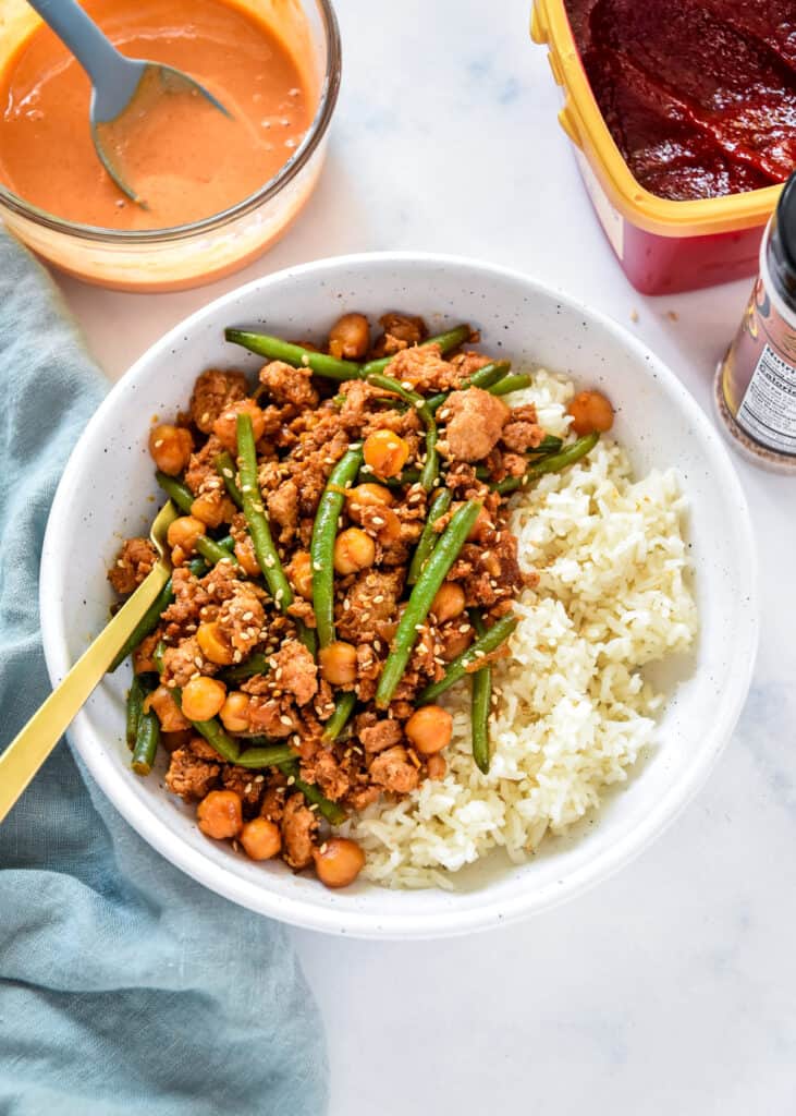 Korean-Inspired Gochujang Meat And Beans in a white bowl with rice and a fork.
