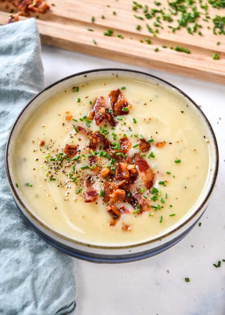 creamy potato onion soup in a bowl with bacon bits and chopped chives on top.