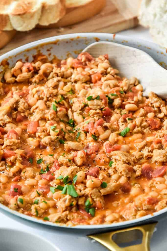 a cooked pan of sloppy ground turkey white bean skillet with a wooden spoon.