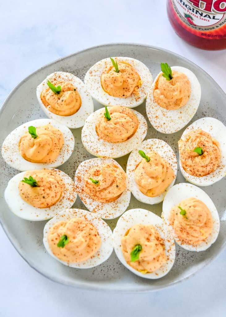 a plate of buffalo deviled eggs with paprika and celery leaves on top.