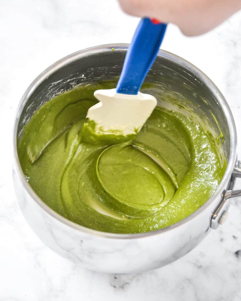 green melted marshmallows and butter in a saucepan being stirred by a silicone spatula.