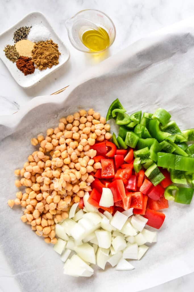 chickpeas, bell peppers and onions on a sheet pan lined with parchment paper.