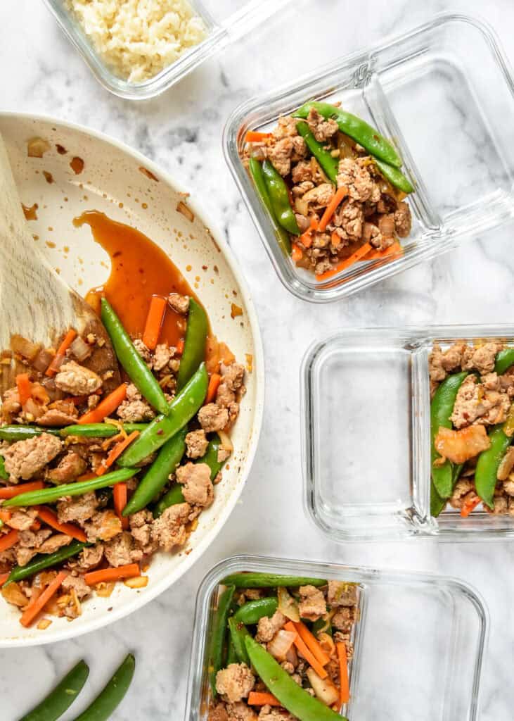 portioning the ground turkey stir fry bowls into meal prep containers with rice.