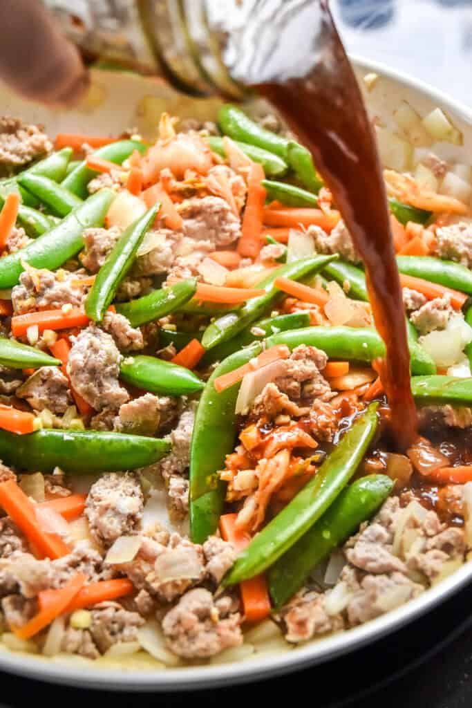 pouring sauce into the stir fry pan.