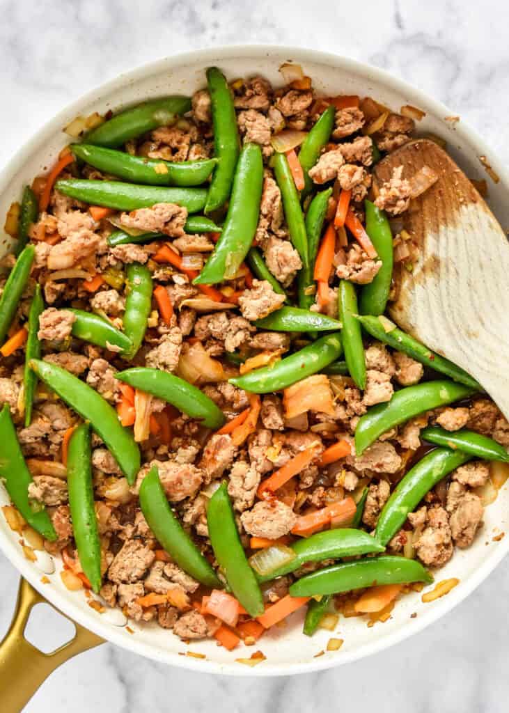 pan of cooked meal prep ground turkey stir fry bowls with wooden spatula.