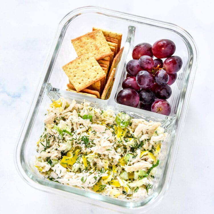 zesty pepperoncini chicken salad with crackers and grapes in a glass meal prep container.