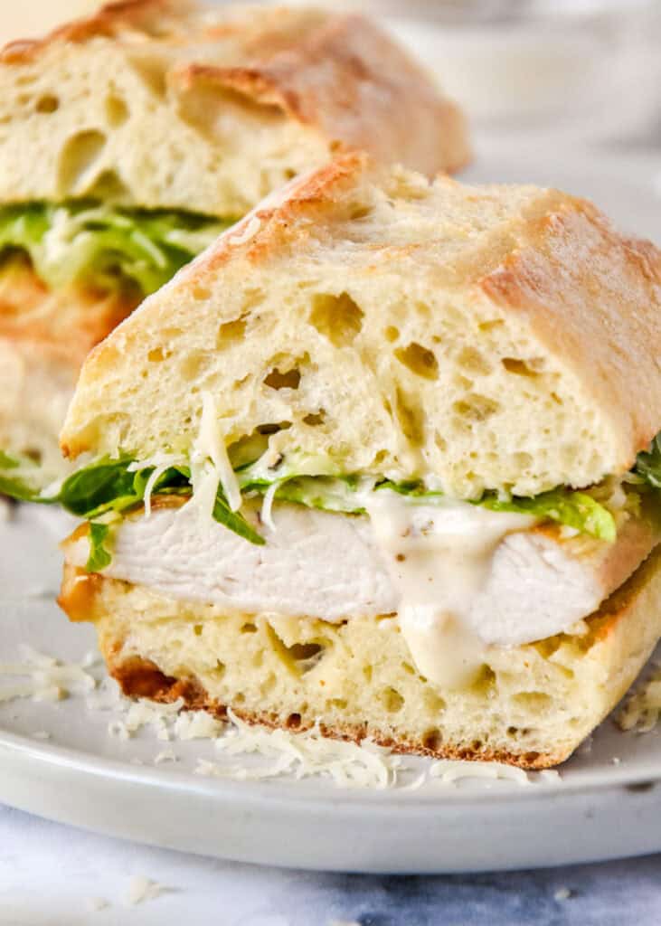 caesar salad chicken sandwiches on a plate cut in half with dressing dripping.