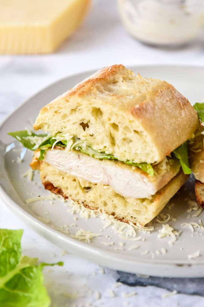 caesar salad chicken sandwich on ciabatta roll cut in half.