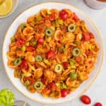 loaded bloody mary pasta salad in a white bowl with green olives on top.