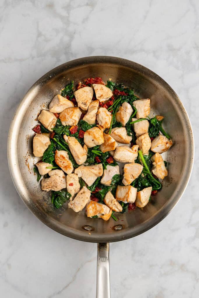 browned chicken pieces and spinach in a stainless steel skillet.